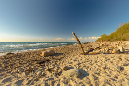 A closeup of rocks on a sandy beach with a sea and a blue sky in the background
