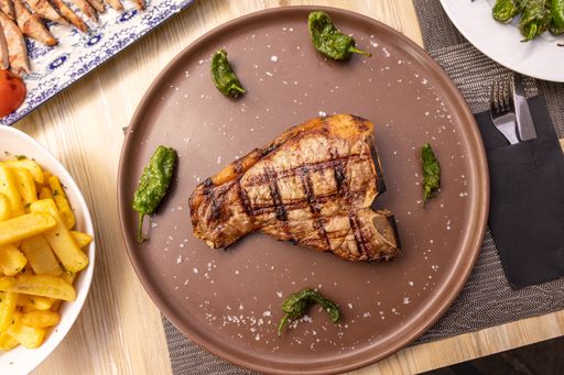 A top view of grilled T-bone steak with chilis served with brown plate in restaurant
