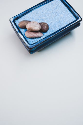 A vertical shot of pebbles on a rectangular box filled with small blue rocks on white background