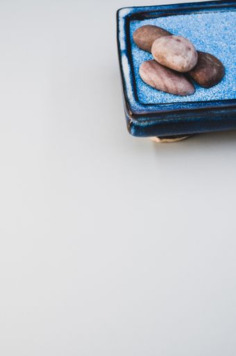 A vertical shot of pebbles on a rectangular box filled with small blue rocks on white background