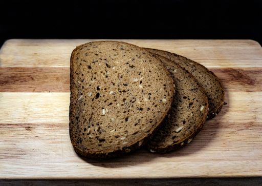 A closeup shot of slices of rye  bread on a wooden chopping board with a black background