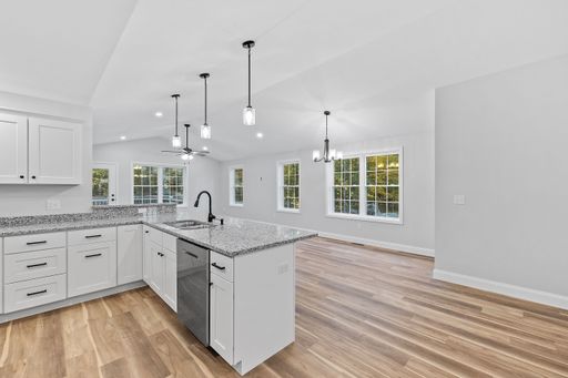 A newly renovated kitchen with hardwood floors, white furniture, silver appliances and a marble island