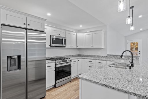 A newly renovated kitchen with hardwood floors, white furniture, silver appliances and a marble island