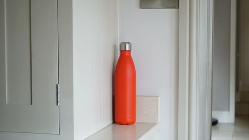 A closeup shot of a red water bottle on a white shelf