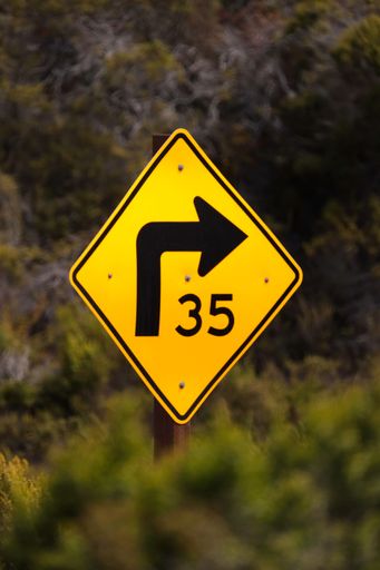 A yellow curved sign with an advisory speed against a blurred background