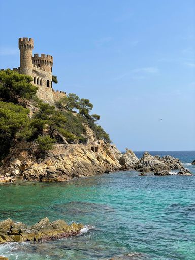 An aerial view of sea waves breaking beach with lloret de Mar castle