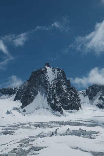A vertical aerial view of rocky Alpine mountain peak with seracs in the foreground and blue cloudy sky