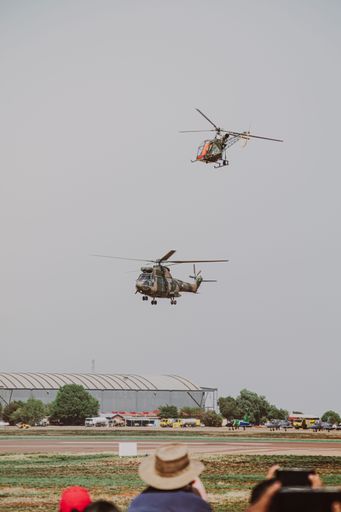 A vertical shot of French combat helicopters in a gloomy gray sky during an air show in Pretoria, South Africa with spectators watching below