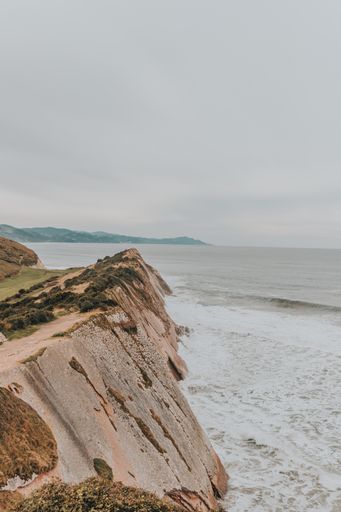 A vertical shot of cliffs surrounded by the sea under a cloudy sky - great for wallpapers