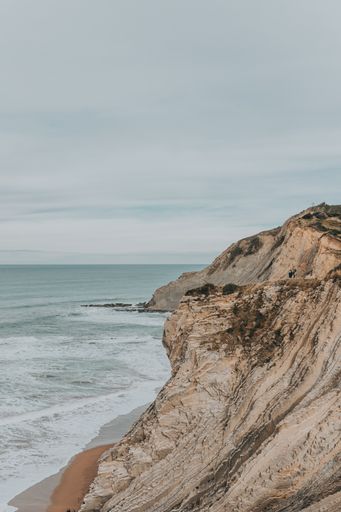 A vertical shot of cliffs surrounded by the sea under a cloudy sky - great for wallpapers
