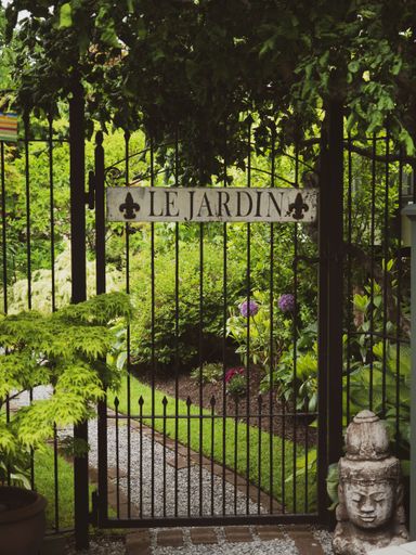 A vertical shot of a metal gate with the French words 'Le Jardin' - Translation: The Garden