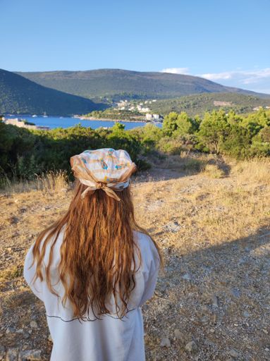 A closeup shot of a girl with brown hair from the back looking at sea view with mountains