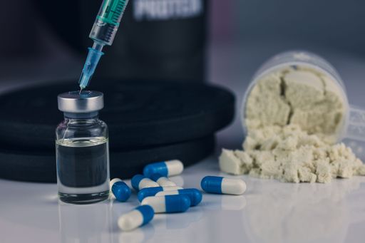 A syringe injected into a vial of steroids with whey powder and pills beside it in a gym - illegal doping concept