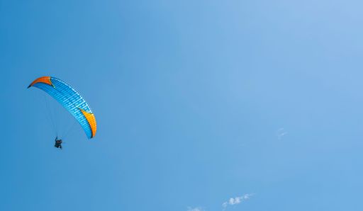 Against of blue summer cloudy sky, paraglider athlete flies on blue-yellow ultralight aircraft - paraglider. Extreme sport and recreation.