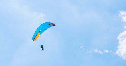 Against of blue summer cloudy sky, paraglider athlete flies on blue-yellow ultralight aircraft - paraglider. Extreme sport and recreation.