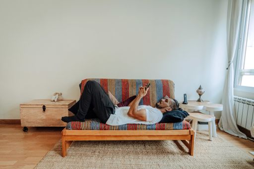A Hispanic man lying on the couch with a smartphone in his hands and relaxing