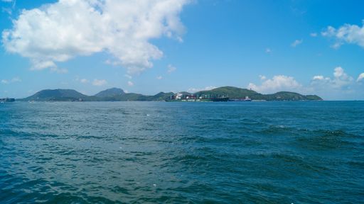 Horizontal view of sea with a container ship with mountains under the blue sky with clouds