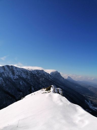 A vertical shot of snow-covered mounts seen from the edge of a hill