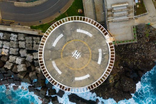 An overhead shot of helicopter landing pad on the edge of the cliff by the ocean waves