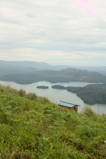 A vertical shot of a building over a river against the scenic green hills