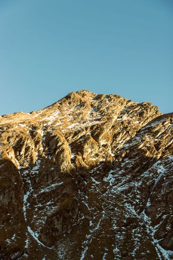 A vertical shot of a mountain covered in snow under the clear sky