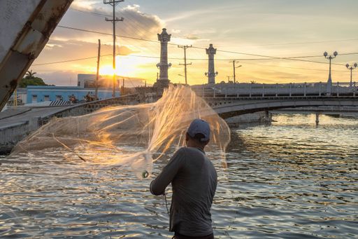 A Fisherman throwing fishing net during sunrise
