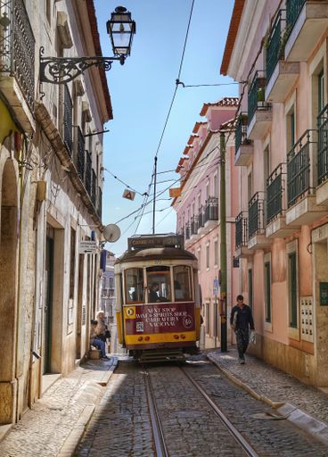 A vertical shot of a cable going through a narrow alley surrounded by buildings under a sunny sky in Lisbon, Portugal