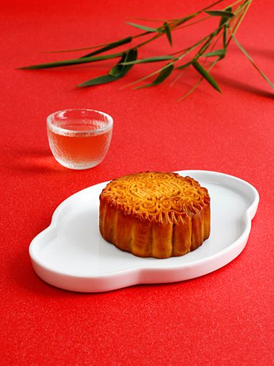 A vertical shot of a mooncake in a white plate and a glass of tea on red background