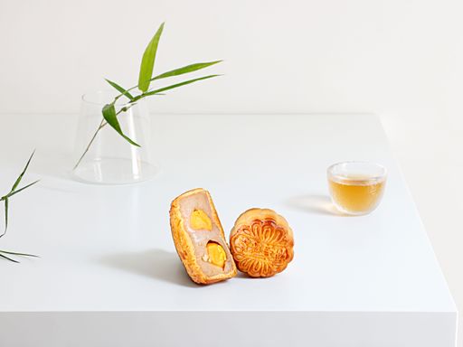 A close-up shot of a mooncake, a teacup and a decorative plant on a white table