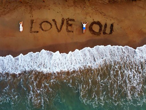 Two lovers relaxing on the beach, with a romantic message "love you" written on the sand