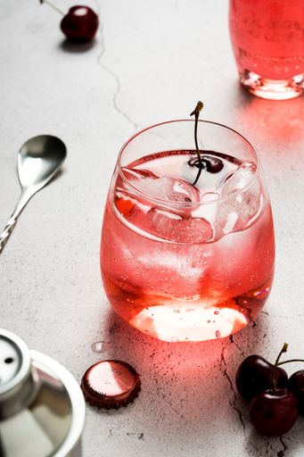 A vertical top view of glass of shirley temple cocktail and cherries on a white table