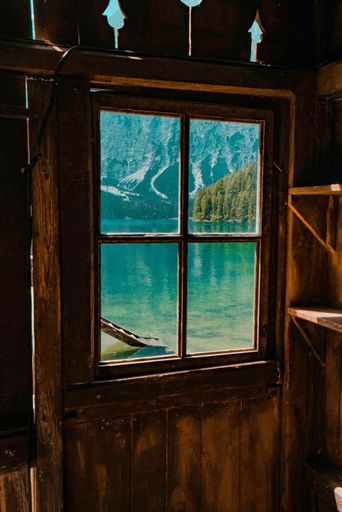 A vertical shot of beautiful lake and nature seen behind the windows of a wooden cabin