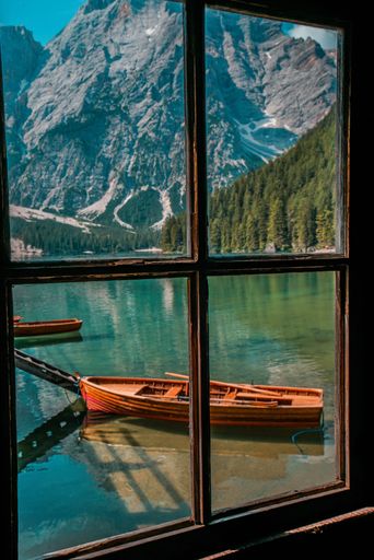 A small wooden boat in the lake and beautiful nature seen behind the windows of a cabin