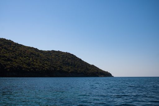 A beautiful shot of bright blue water near a coast with tree-covered hills