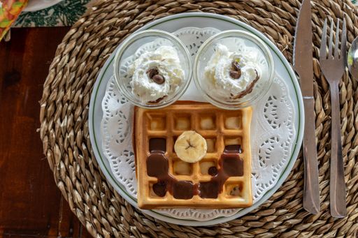 A top view of a breakfast plate with a chocolate covered waffle and cream