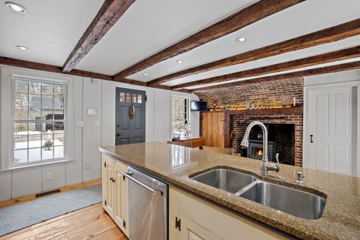 A nicely furnished sink with beige cabinets separating the kitchen from a room with fireplace