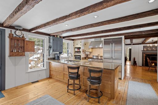 A nicely furnished bar stools and a counter with in a kitchen with brick fireplace seen behind