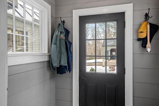 The winter jackets hang next to a front door with a window looking out to the snow-covered street