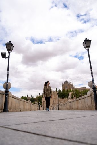 A vertical shot of a Young woman on a bridge with beautiful buildings in the background