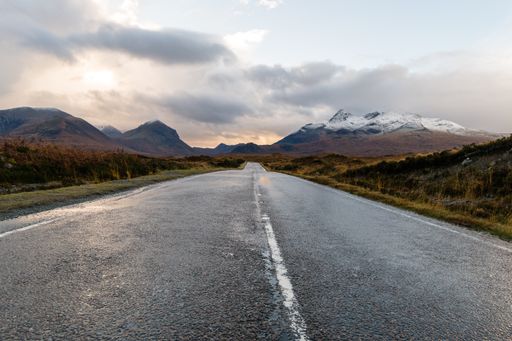 A paved road winding through a dry grass-covered landscape with a mountain range on the horizon