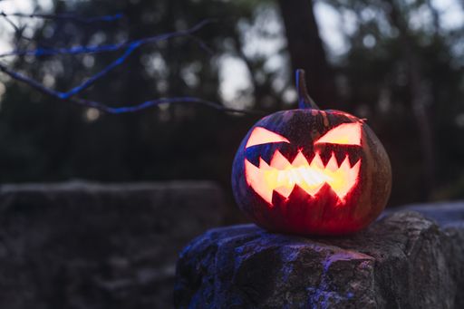 A Halloween pumpkin with a scary face on a rock in a forest