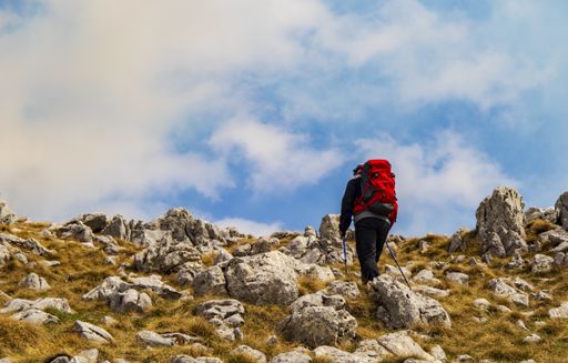A person with a backpack hiking in the rocky mountains under a cloudy sky