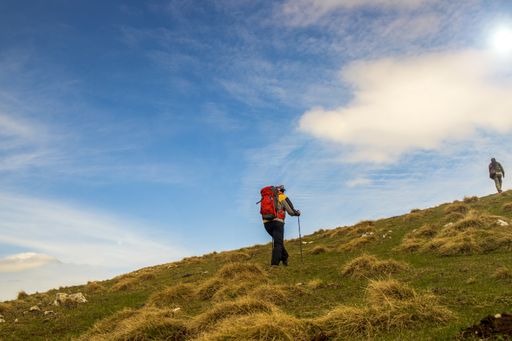 A person with a backpack hiking in the rocky mountains under a cloudy sky