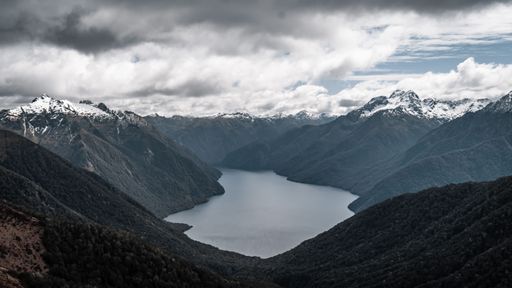 A scenic shot of a lake surrounded by mountains and valleys under a cloudy sky