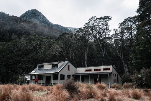 A scenic shot of a house in the middle of a field with dry grass and trees on the base of a mountain