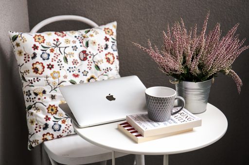 A Macbook sat on a table next to a cup of coffee, a stack of books and a flower pot