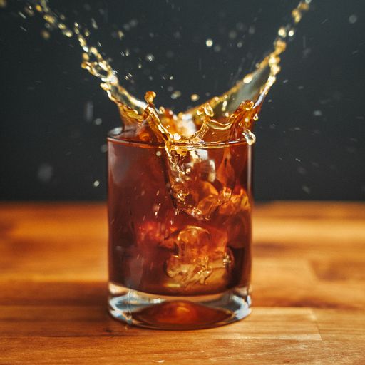 A closeup shot of ice splashing into a glass of brown coffee