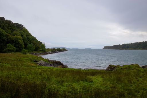 A breathtaking view of the Oban Coast in Scotland, featuring lush rolling hills, a calm blue sea, and a bright blue sky