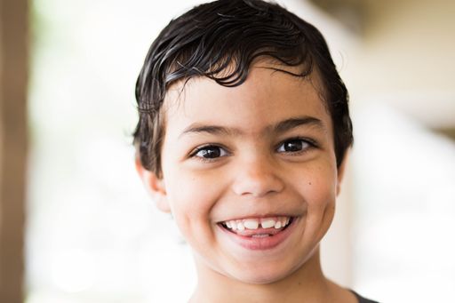 A closeup of a cute young Caucasian boy with wet hair smiling and looking at a camera