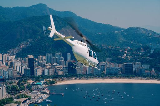 A white Bell Jet Ranger helicopter taking off over Enseada de Botafogo, Rio de Janeiro City for a sight tour, daylight, warm color, blue
